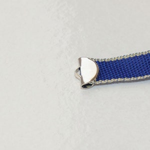 Puede incluir: Primer plano de una cinta azul y blanca con un cierre de metal plateado. La cinta está tejida con una textura fina.