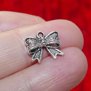 Pode incluir: Um amuleto de laço prateado com acabamento texturizado. O amuleto tem um laço na parte superior para prender a um colar ou pulseira.