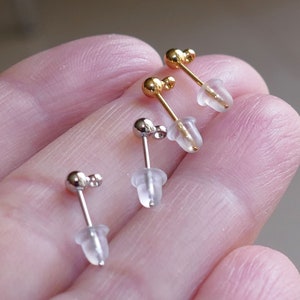 May include: Three pairs of stud earrings with clear plastic backs. Two pairs are gold and one pair is silver.