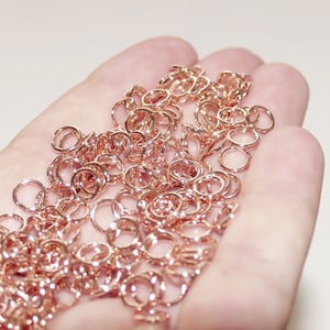 Könnte beinhalten: Ein großer Haufen roségoldener Sprungringe. Die Ringe sind klein und filigran, perfekt für die Schmuckherstellung.