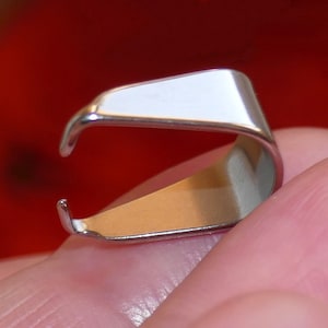 May include: A polished, silver-coloured metal pendant bail, designed for holding a pendant. The bail features a curved, open design with a flat top and a rounded base. The background is a solid red colour.