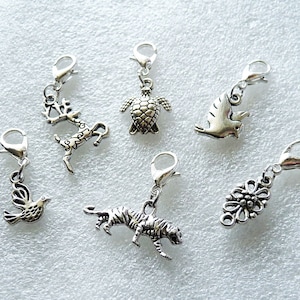 May include: Six silver charm pendants with different designs: a deer, a turtle, a bird, a tiger, a flower, and a dove. The charms are all attached to silver rings.