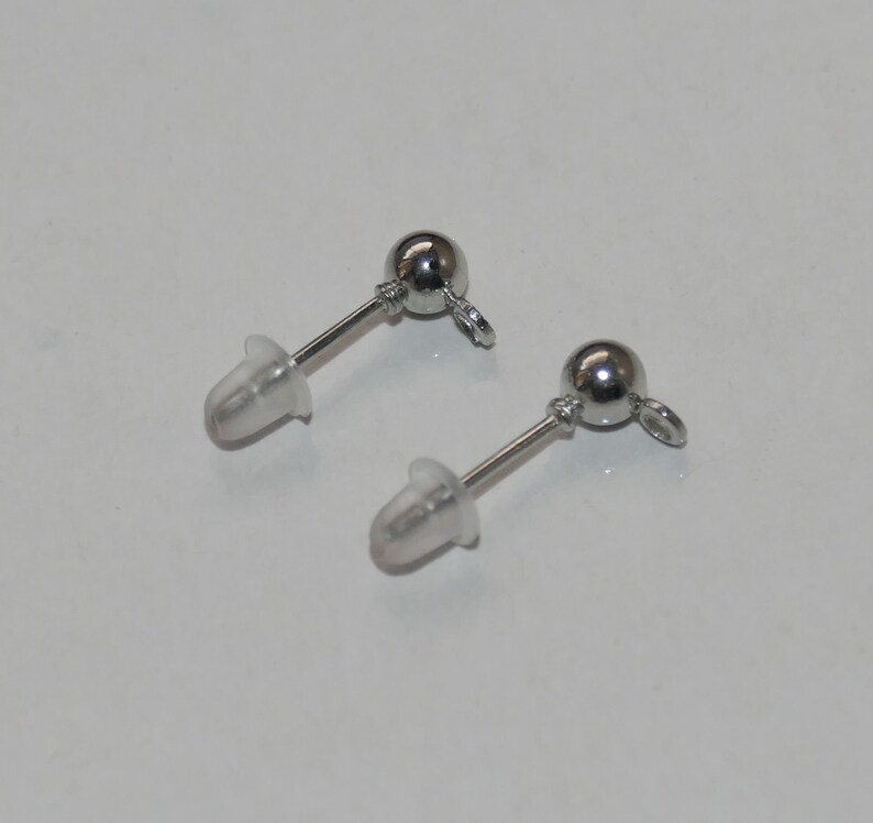 May include: Two silver earring posts with clear rubber backs. The posts have a small silver ball at the top and a loop at the bottom.