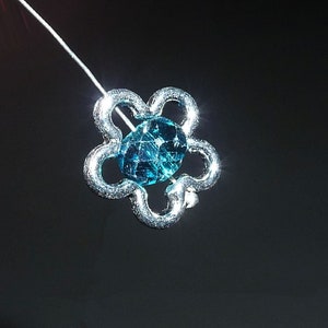 May include: A silver flower charm with a blue gemstone in the center.