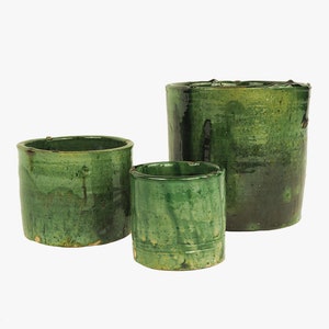 May include: Three green ceramic pots of varying sizes. The pots have a rustic, hand-crafted look with a green glaze and subtle variations in color.
