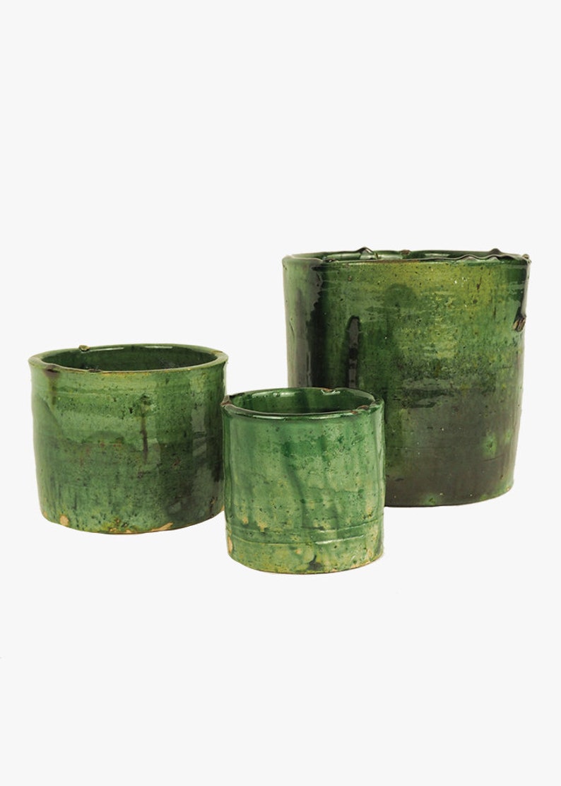 May include: Three green ceramic pots of varying sizes. The pots have a rustic, hand-crafted look with a green glaze and subtle variations in color.
