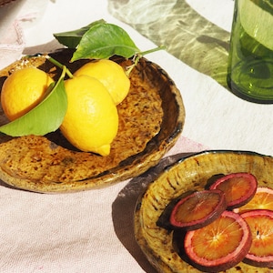 May include: Two ceramic plates, one with three whole lemons and green leaves, the other with sliced red oranges. Both plates have a rustic, brown glaze.