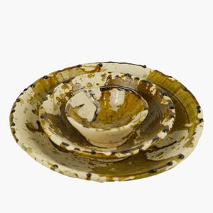 May include: A set of three ceramic bowls in varying sizes. The bowls have a cream-coloured base with olive green and brown accents. The rims are decorated with small, dark brown dots. The bowls are nested together, with the smallest bowl in the centre.