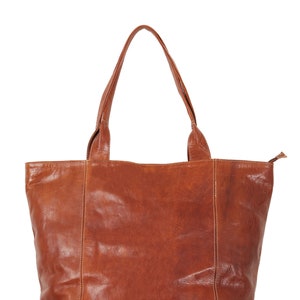 May include: A brown leather tote bag with two top handles. The bag has a zipper closure and a slightly textured surface.