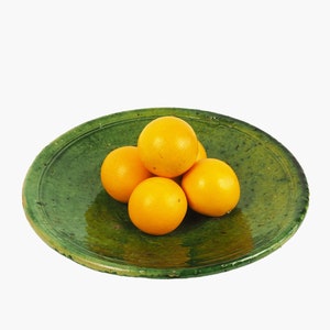 May include: A rustic, green ceramic plate holds five bright orange oranges. The plate has a slightly uneven, aged appearance, with a textured surface. The oranges are round and vibrant, contrasting with the plate's color.