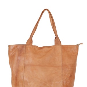 May include: A tan leather tote bag with two handles. The bag has a zipper closure and a slightly distressed look.