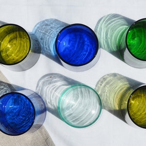 Peut inclure: Six verres en verre de diff&eacute;rentes couleurs, dont bleu, vert et jaune. Les verres sont dispos&eacute;s en cercle sur une surface blanche.