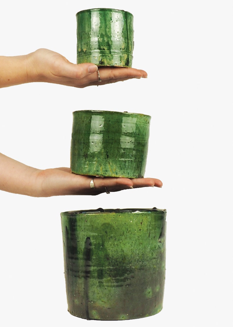 May include: Three green ceramic pots of varying sizes stacked on top of each other. The pots are all glazed in a dark green color with a slightly textured surface.