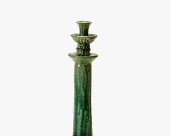 Könnte beinhalten: Ein hoher, grüner Kerzenhalter aus Keramik mit glänzendem Finish. Der Kerzenhalter hat ein mehrschichtiges Design mit breitem Sockel und schmaler Spitze. Die Farbe ist ein tiefes, sattes Grün.