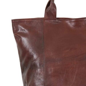 May include: A brown leather tote bag with a single top handle. The bag has a smooth, textured leather finish.