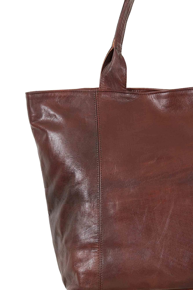 May include: A brown leather tote bag with a single top handle. The bag has a smooth, textured leather finish.