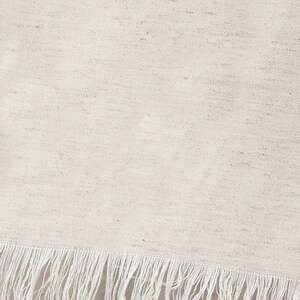 Puede incluir: Primer plano de una tela blanca con un brillo sutil y un borde de flecos blancos.