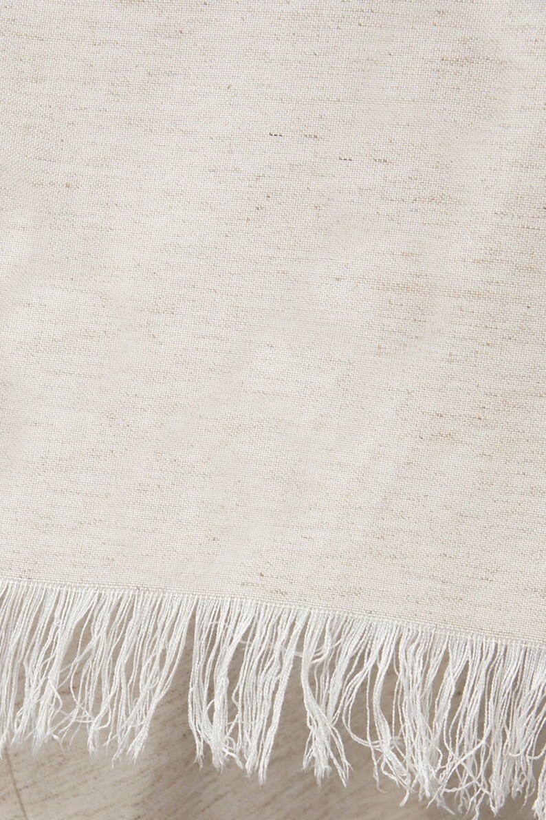 Puede incluir: Primer plano de una tela blanca con un brillo sutil y un borde de flecos blancos.