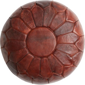 Puede incluir: Un puf de cuero marrón con una parte superior circular y un patrón de forma de diamante. El puf es de estilo marroquí tradicional.