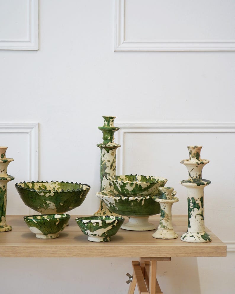 May include: A collection of ceramic bowls and candle holders with a green and white splatter design. The bowls have a ruffled edge. The candle holders are various heights and shapes. The items are displayed on a light wood surface.