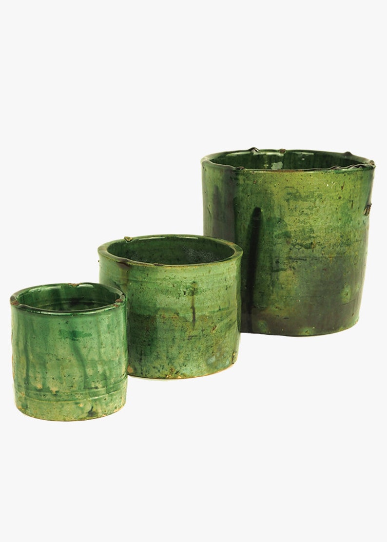 May include: Three green ceramic pots of varying sizes. The pots are glazed in a dark green color with a slightly textured surface.