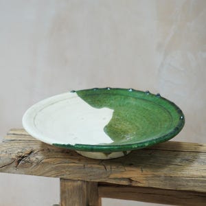 Puede incluir: Un cuenco de cer&aacute;mica hecho a mano con esmalte blanco y verde. El cuenco es redondo y poco profundo. El esmalte verde cubre la mitad del cuenco, y el borde tiene peque&ntilde;os detalles azul oscuro. El cuenco est&aacute; sobre una superficie de madera r&uacute;stica. Di&aacute;metro: aprox. 30 cm.