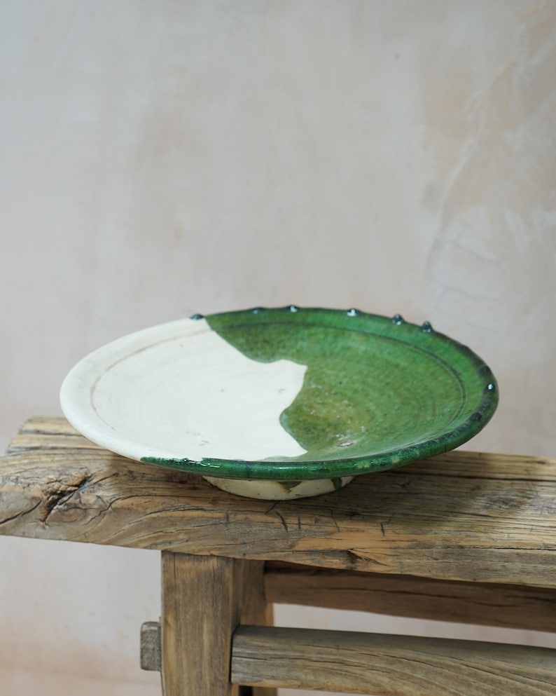 Puede incluir: Un cuenco de cer&aacute;mica hecho a mano con esmalte blanco y verde. El cuenco es redondo y poco profundo. El esmalte verde cubre la mitad del cuenco, y el borde tiene peque&ntilde;os detalles azul oscuro. El cuenco est&aacute; sobre una superficie de madera r&uacute;stica. Di&aacute;metro: aprox. 30 cm.