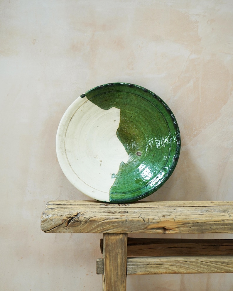 Puede incluir: Un plato de cer&aacute;mica hecho a mano con un dise&ntilde;o &uacute;nico. El plato es mitad blanco y mitad verde, con un acabado brillante. El plato est&aacute; sobre un banco de madera r&uacute;stica. Es un objeto decorativo.