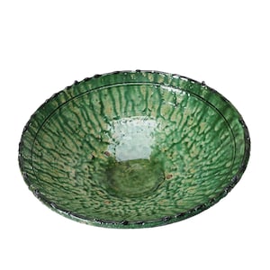 May include: A large, green ceramic bowl with a textured surface and a slightly raised rim. The bowl has a glossy finish and is decorated with a subtle pattern of green and brown.