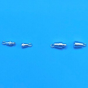 May include: Four silver-toned metal clasps for jewelry making. Two are small and round with a loop on one end. The other two are larger and cylindrical with a loop on each end.