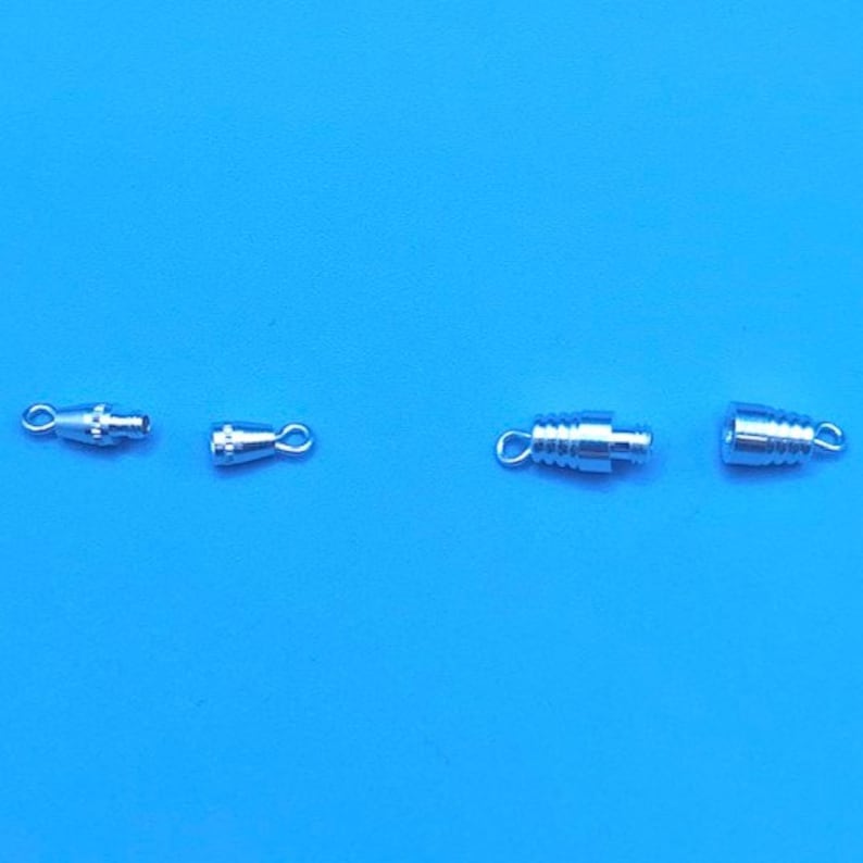 May include: Four silver-toned metal clasps for jewelry making. Two are small and round with a loop on one end. The other two are larger and cylindrical with a loop on each end.