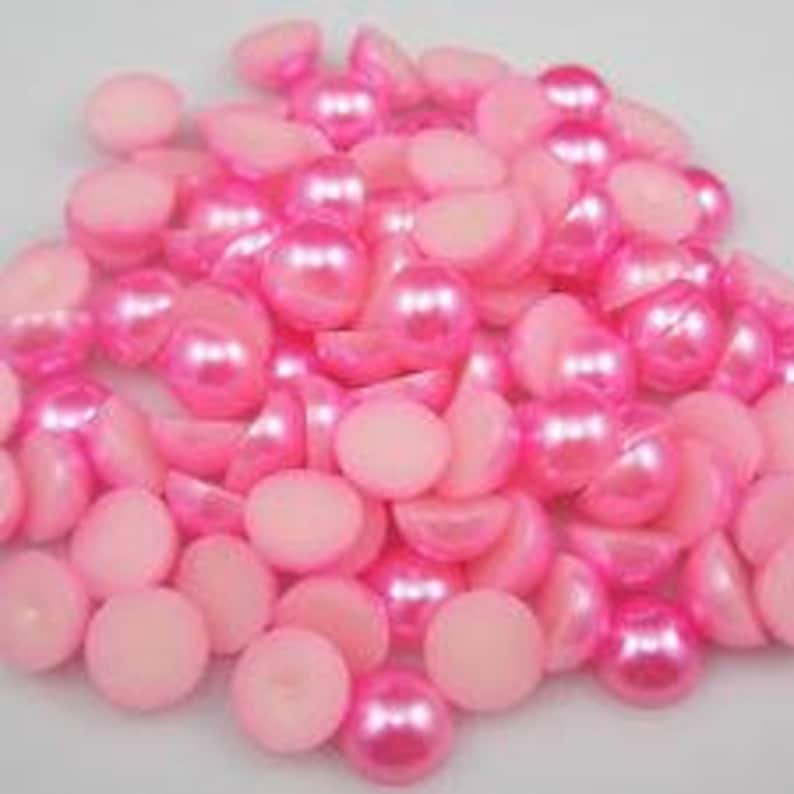 May include: A large pile of pink pearl-like buttons. The buttons are round and have a smooth, shiny finish.