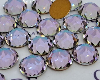 Pode incluir: Um close-up de um monte de strass de vidro transparente e iridescente. Os strass têm um design facetado e estão espalhados sobre uma superfície branca.