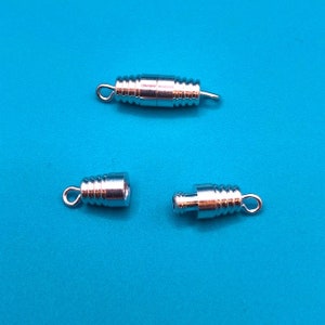 May include: Three silver-toned metal clasps for necklaces or bracelets. The clasps are cylindrical and have a threaded design. They are designed to be used with a cord or chain.