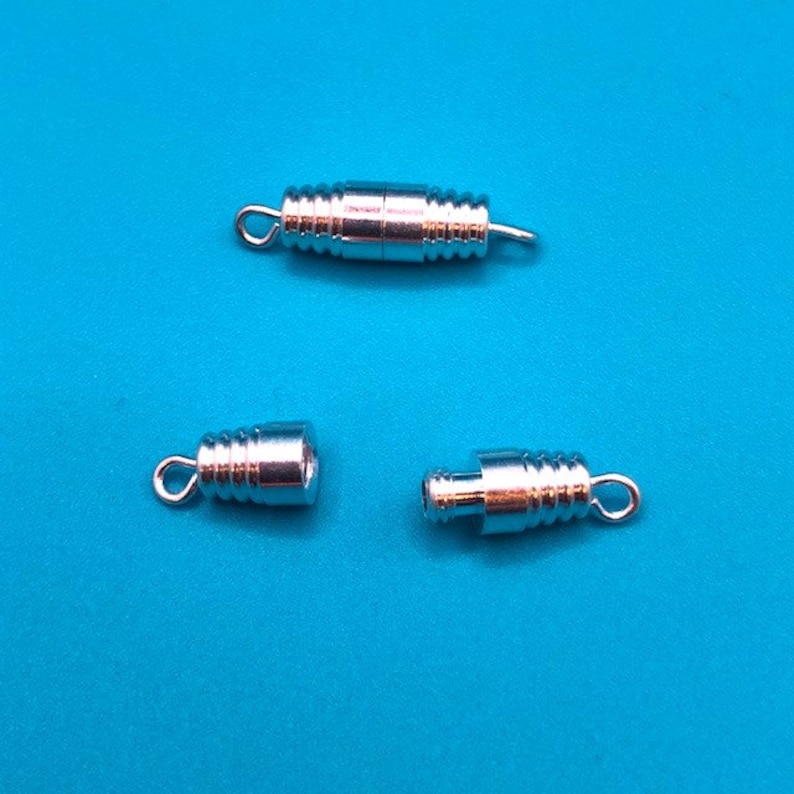 May include: Three silver-toned metal clasps for necklaces or bracelets. The clasps are cylindrical and have a threaded design. They are designed to be used with a cord or chain.