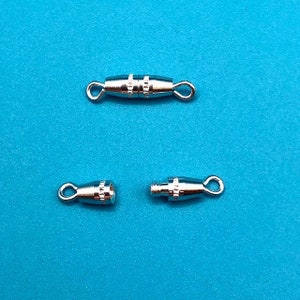 May include: Three silver-toned metal clasps for jewelry making. The clasps are designed to be used with a cord or chain. The clasps are shown on a blue background.