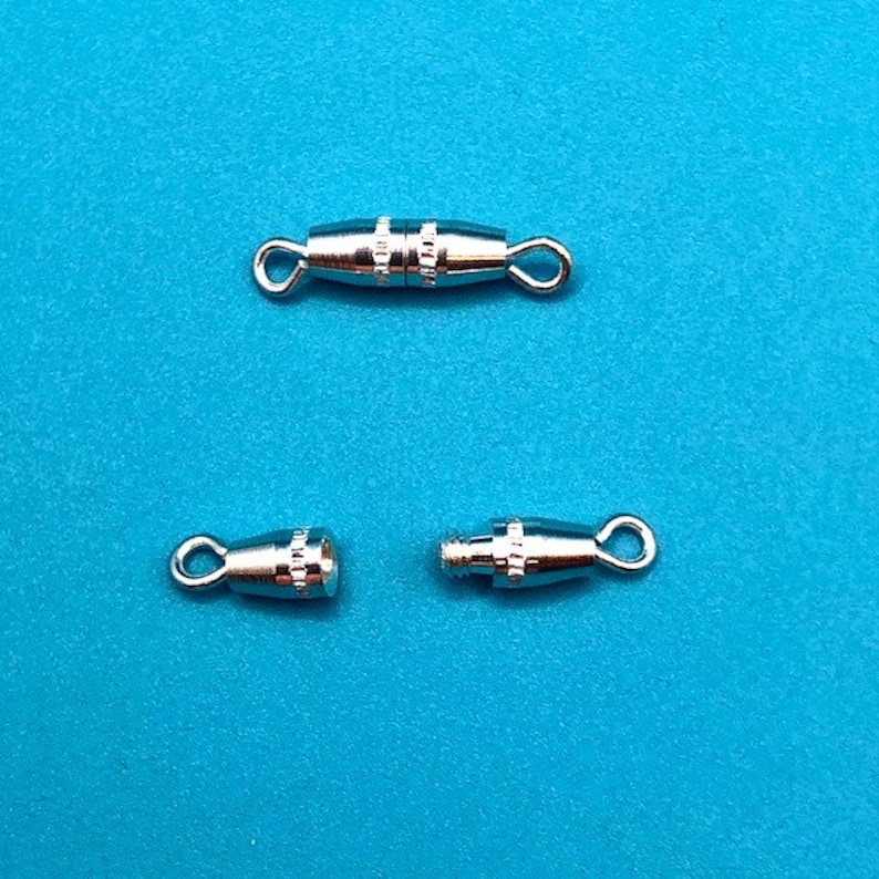 May include: Three silver-toned metal clasps for jewelry making. The clasps are designed to be used with a cord or chain. The clasps are shown on a blue background.