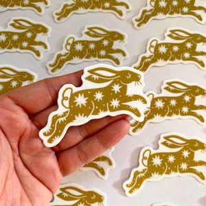 May include: A sheet of gold foil stickers featuring a stylized illustration of a running rabbit with a white star pattern. The rabbit is facing right and has long ears.