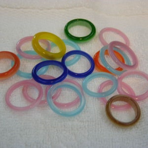 May include: Assortment of colourful glass rings in various shades of blue, pink, green, yellow, and orange. The rings are made of smooth, polished glass and are perfect for stacking or wearing individually.