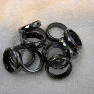 May include: A group of black gemstone rings, stacked and overlapping. The rings are faceted and have a shiny, polished finish.