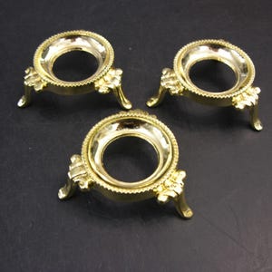May include: Three gold metal decorative stands with a round top and three legs. The stands are designed to hold a sphere or orb.
