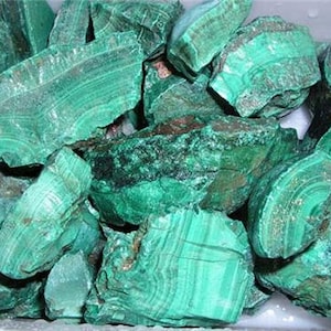 May include: A collection of raw malachite stones in various sizes and shapes. The stones are a vibrant green color with intricate patterns and striations.