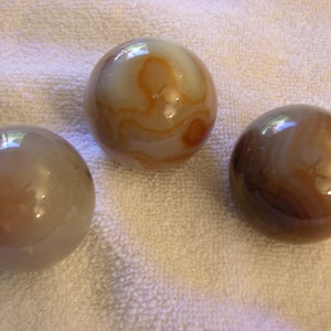 May include: Three agate spheres, each with a different pattern of brown and white swirls. The spheres are smooth and polished.