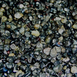 Puede incluir: Una imagen de primer plano de una colección de pequeñas piedras de color gris oscuro, negro y azul. Las piedras son lisas y tienen una variedad de formas y tamaños.