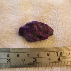 May include: A purple and black crystal rock with a rough, irregular shape. The rock is about 2 inches long and 1 inch wide.