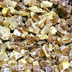 May include: A close-up view of a pile of amber-colored, irregularly shaped gemstones. The stones vary in size and have a translucent quality, with some reflecting light. The overall color palette is a mix of golden yellow and brown.