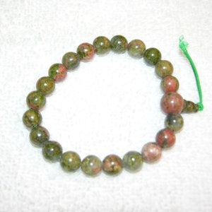 May include: A green and pink speckled stone bracelet with a green elastic cord.