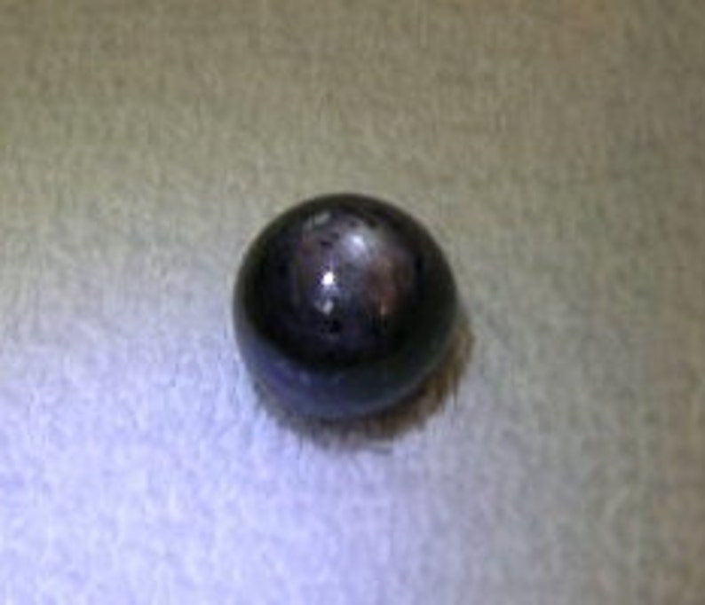 May include: A single, smooth, spherical bead with a dark, polished black surface. The bead features a distinct, reflective highlight on its top, indicating a glossy finish. The object is round and uniform in shape, presenting a solid, dark appearance.