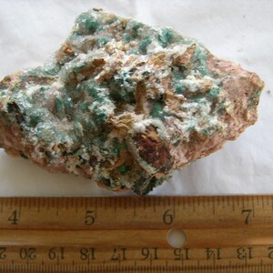 May include: A close-up of a green and pink rock with a rough texture. The rock is about 6 inches long and 4 inches wide.