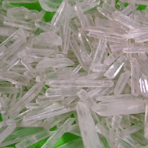 Może przedstawiać: Zbliżenie na stos przezroczystych kryształów kwarcu. Kryształy są długie i smukłe, ze spiczastym końcem. Są ułożone w przypadkowy wzór, niektóre nakładają się na siebie.